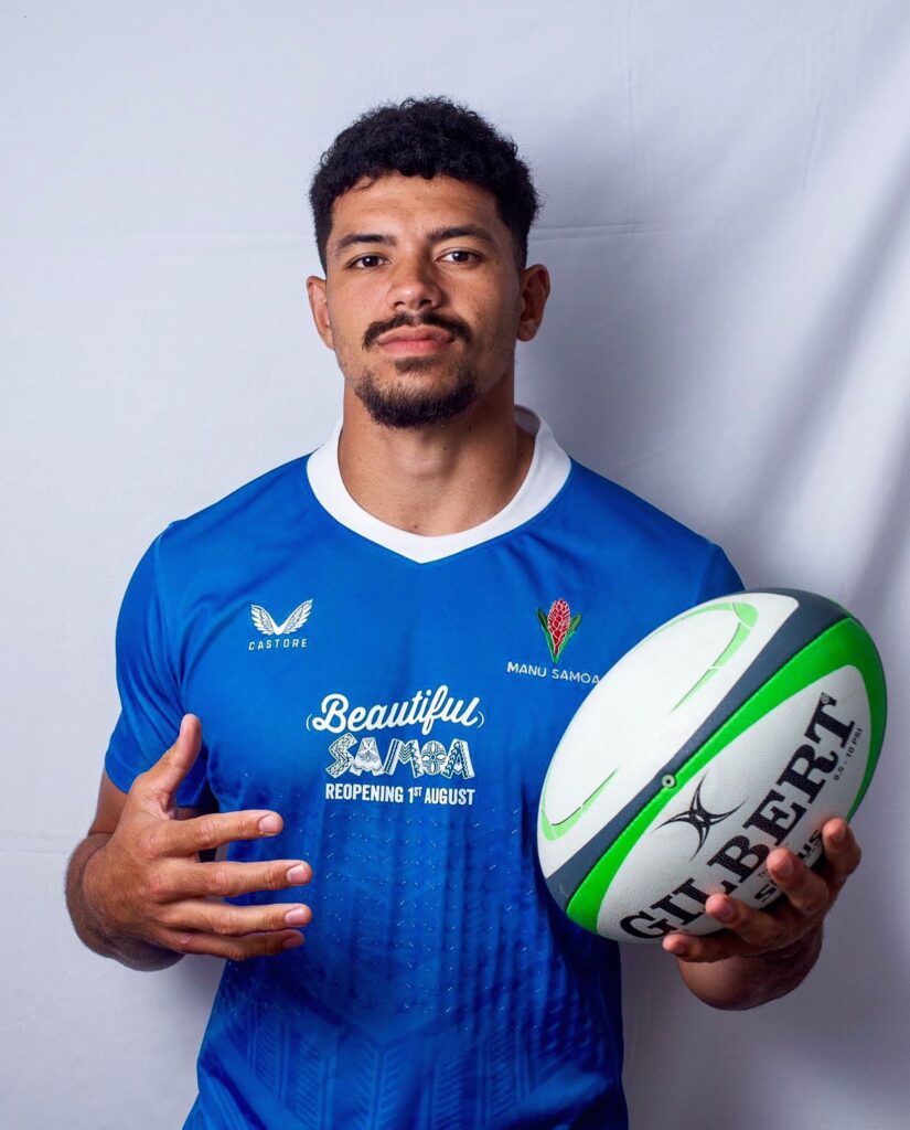 Theo McFarland, Manu Samoa rugby player, poses in a blue jersey holding a green and white Gilbert rugby ball in front of a white backdrop.