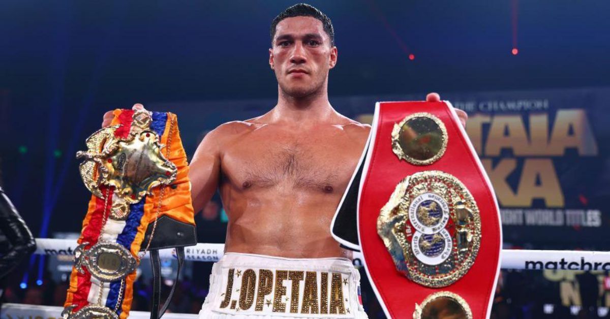 Jai Opetaia standing in a boxing ring holding the IBF and The Ring cruiserweight world title belts.