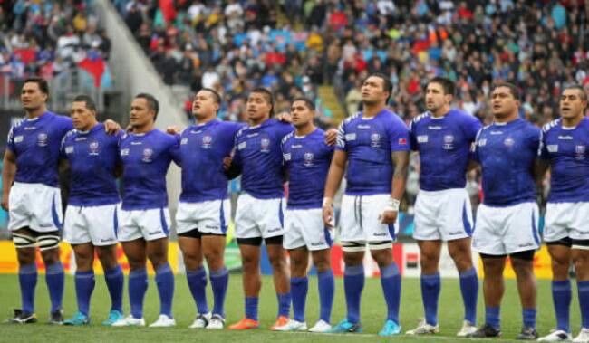 Members of the Manu Samoa national rugby team standing in a line with arms around each other on the pitch during a match.