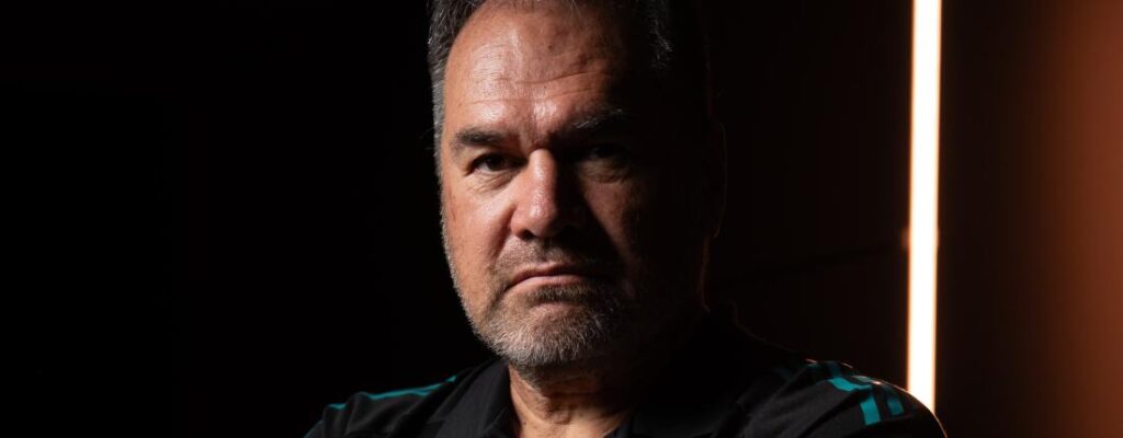 Close-up portrait of rugby coach Dave Rennie against a dark background with dramatic lighting.