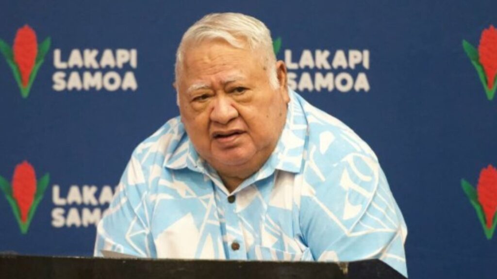 tuilaepa Sailele Malielegaoi speaking at a Lakapi Samoa event in front of a blue background with Samoa Rugby logos."