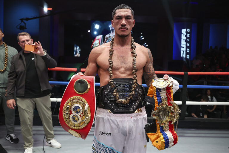 Professional boxer Jai Opetaia standing in a boxing ring holding IBF and Zuffa Boxing championship belts.