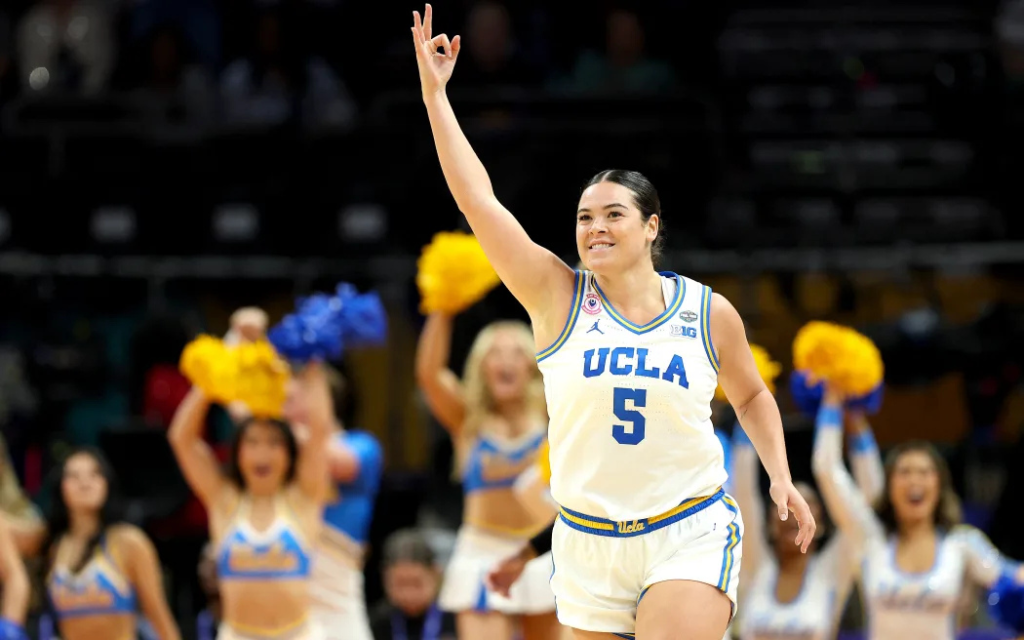 UCLA Bruins guard Charlisse Leger-Walker celebrating on court during a college basketball game with cheerleaders in the background.