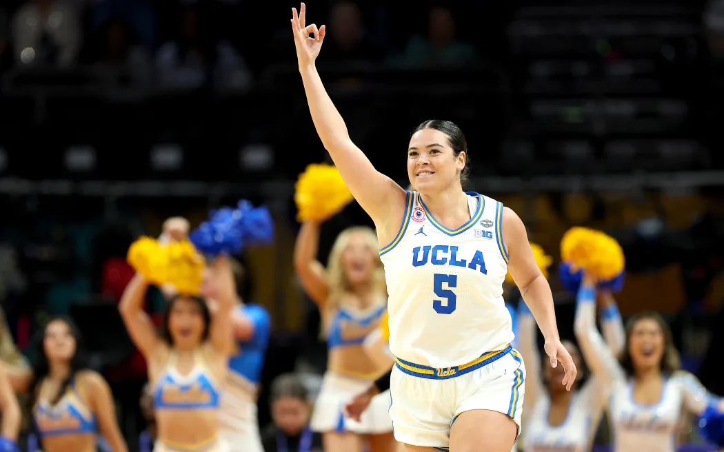 UCLA Bruins guard Charlisse Leger-Walker celebrating on court during a college basketball game with cheerleaders in the background.
