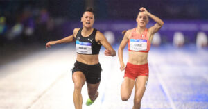 New Zealand sprinter Zoe Hobbs in a black uniform pulling ahead of Canada's Audrey Leduc on a rain-slicked track during the women's 100m final at the Commonwealth Games.