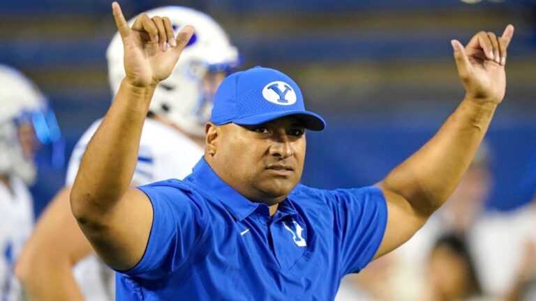 BYU football head coach Kalani Sitake raises both arms on the sideline during a game.