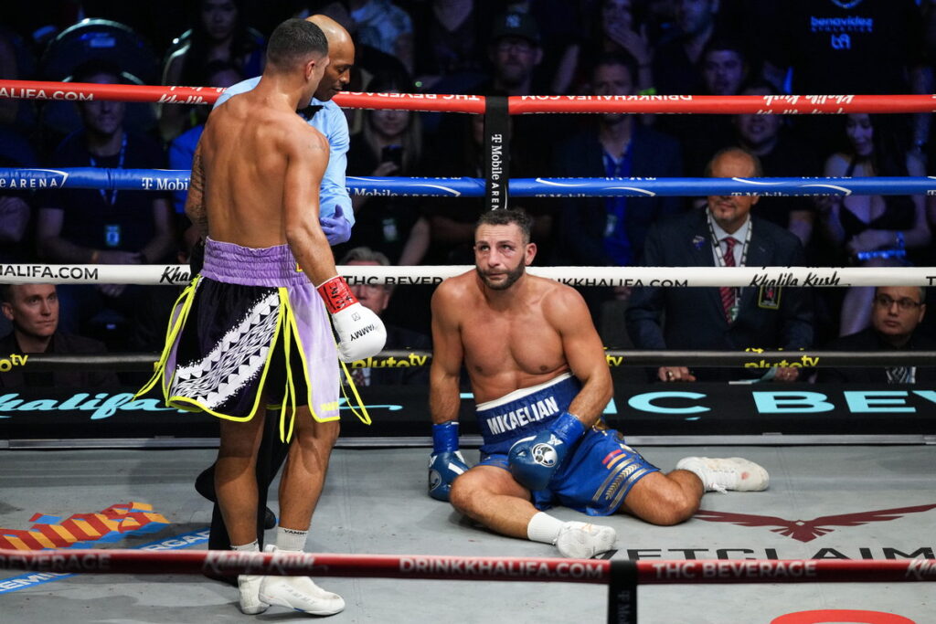 Noel Mikaelian sits on the canvas as referee Harvey Dock waves off the fight in the ninth round