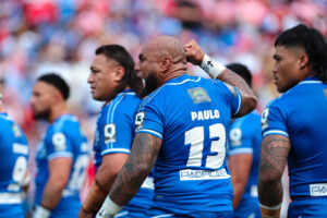 oa Samoa forward Junior Paulo raises his fist while standing with teammates in blue jerseys during game day in Brisbane.